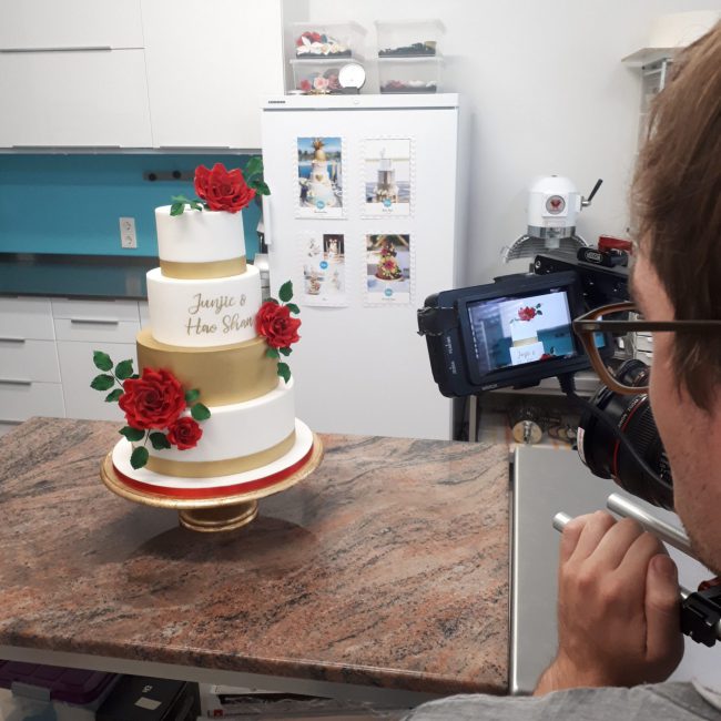 Kameramann von hinten, der eine vierstöckige Hochzeitstorte film in der Küche des Tortenstudios