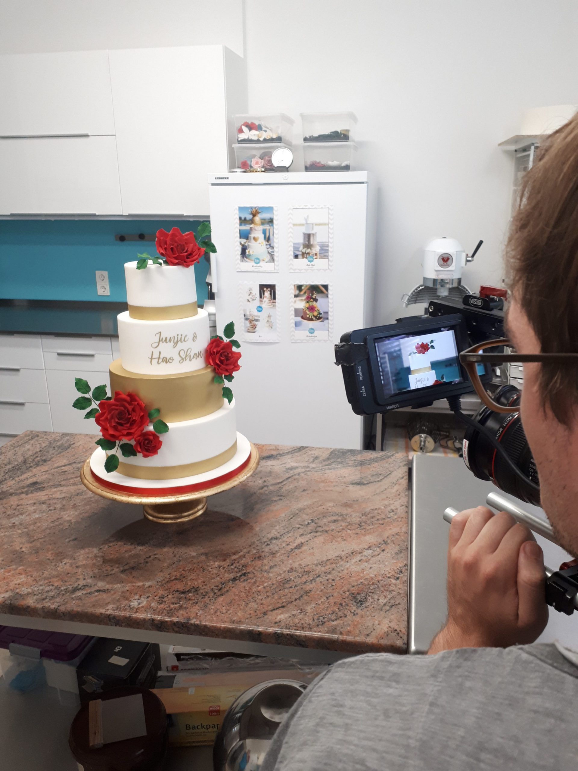 Kameramann von hinten, der eine vierstöckige Hochzeitstorte film in der Küche des Tortenstudios