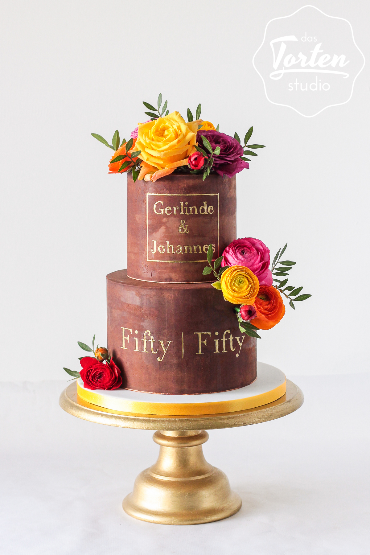 zweistöckige Geburtstagstorte aus Schokolade, dekoriert mit bunten Rosen und Ranunkel, Aufschrift in Gold