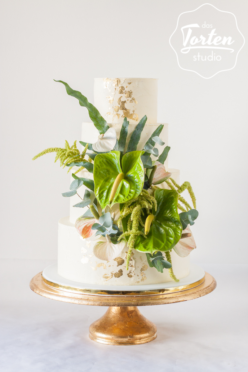 vierstöckige Buttercremetorte mit Streifenoptik, dekoriert mit tropischen Pflanzen und Blattgold