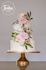Hochzeitstorte mit Buttercreme in Streifenoptik, dekoriert mit einer Kaskade aus Blumen in Blush, Weiß und Rosa - Blushing bridal Protea, Pfingstrose & Olivenzweige