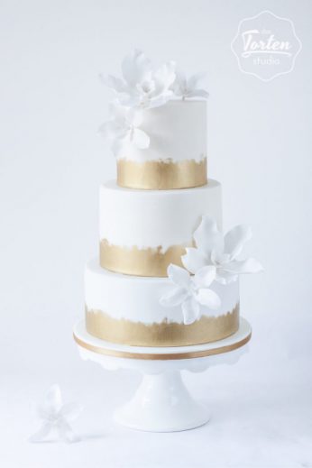 Dreistöckige weiße Torte, Gold gemalt am Fuß der Etagen, dekoriert mit weißen Zuckerblumen