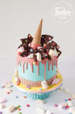 Türkise Buttercreme-Torte mit rosa Schokodrip, dekoriert mit Marshmellwos, Schokosplitter, Smarties, Streusel und Eistüte