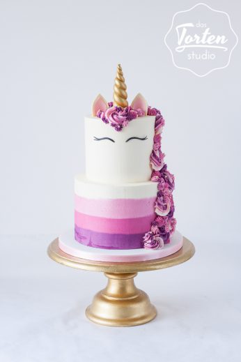 zweistöckige Einhorn-Torte in Rosa, Pink und Lila, goldenes Horn, geschlossene Augen, gespritzte Buttercreme-Mähne