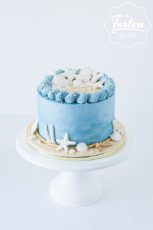 Einstöckige Buttercremetorte in Hellblau, dekoriert mit Zuckermuscheln und Seesternen und essbarem Sand