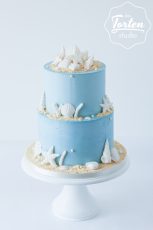 zweistöckige blaue Buttercreme-Torte, dekoriert mit essbaren Muscheln und Meeresfrüchten, Perlen und essbarem Sand