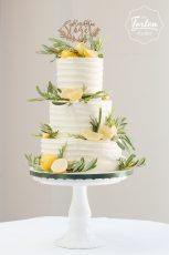 Dreistöckige Buttercreme-Torte in Streifenoptik, dekoriert mit echten Zitronen, Rosmarin und Olvenblättern