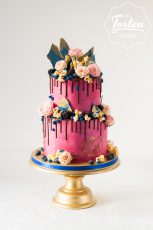 Pink Buttercreme-Torte mit Schokodrip, dekoriert mit Salted Caramel Popcorn, kleinen Rosen, dunklen Beeren, blauen Schokosegel und Buttercremetupfen