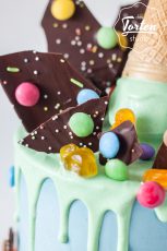 Detailaufnahme von 2-stöckige, hellblaue Buttercremetorte mit hellgrünem Schokodrip, dekoriert mit Eistüte, Schokosplittern, Smarties und anderen Süßigkeiten