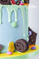 2-stöckige, hellblaue Buttercremetorte mit hellgrünem Schokodrip, dekoriert mit Eistüte, Schokosplittern, Smarties und anderen Süßigkeiten