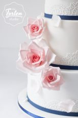 Ausschnitt von Dreistöckige Hochzeitstorte in Weiß, dekoriert mit essbarer Spitze und Zuckerrosen in Rosa