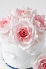 Ausschnitt von Dreistöckige Hochzeitstorte in Weiß, dekoriert mit essbarer Spitze und Zuckerrosen in Rosa