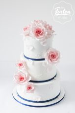 Dreistöckige Hochzeitstorte in Weiß, dekoriert mit essbarer Spitze und Zuckerrosen in Rosa