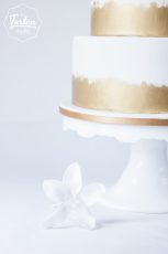 Ausschnitt von Dreistöckige weiße Torte, Gold gemalt am Fuß der Etagen, dekoriert mit weißen Zuckerblumen