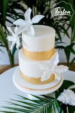 Zweistöckige weiße Torte, Gold gemalt am Fuß der Etagen, weiße Zuckerblumen